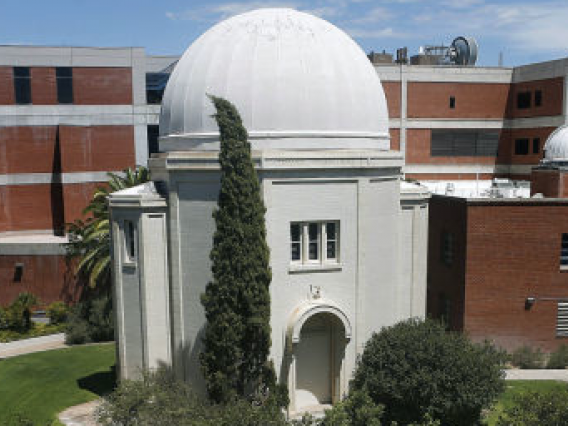 A white observatory dome in the foreground and brick buildings in the background