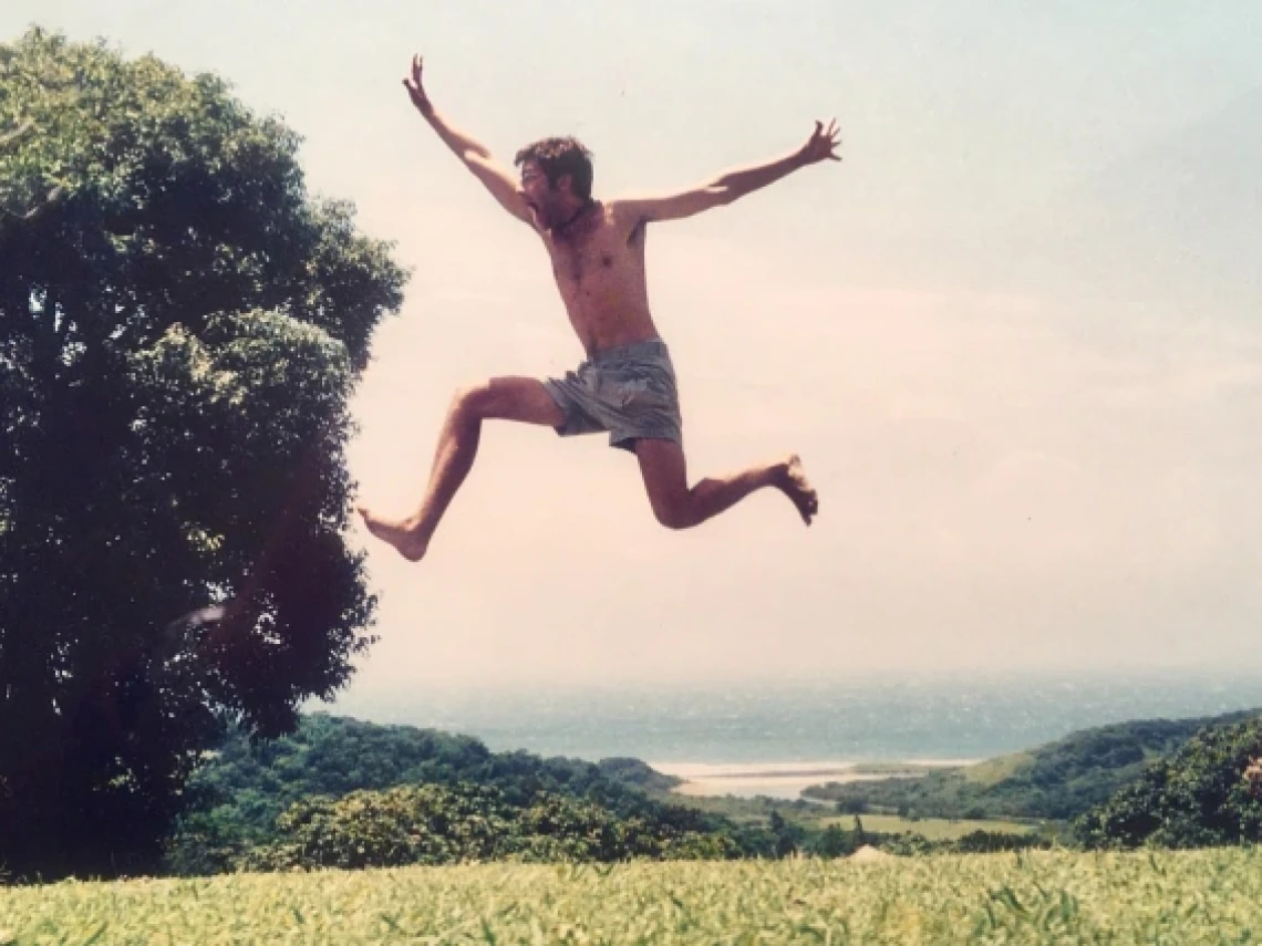 man in glasses taking a big leap in a grassy field