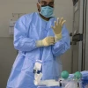 A health care worker in full personal protective equipment (PPE), including a surgical mask, gown, and gloves, prepares to administer care.