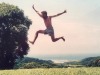 man in glasses taking a big leap in a grassy field